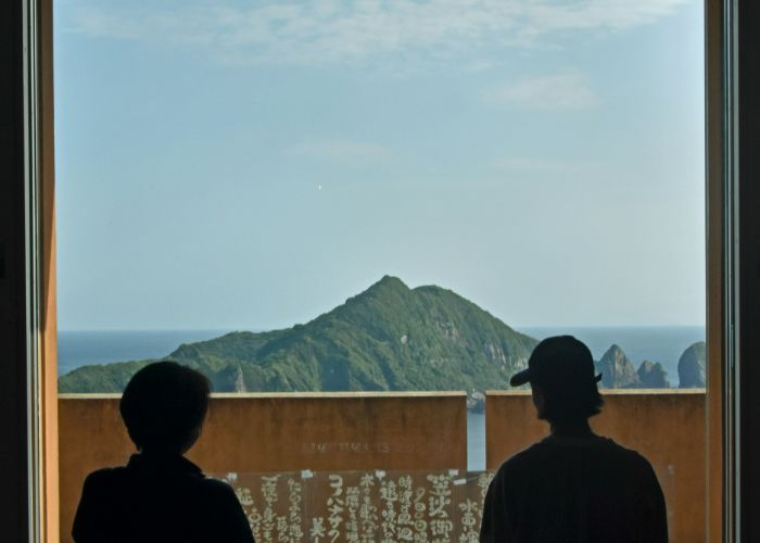 Two people relaxing on their balcony in Kyushu, Japan, staring out at the mountains.